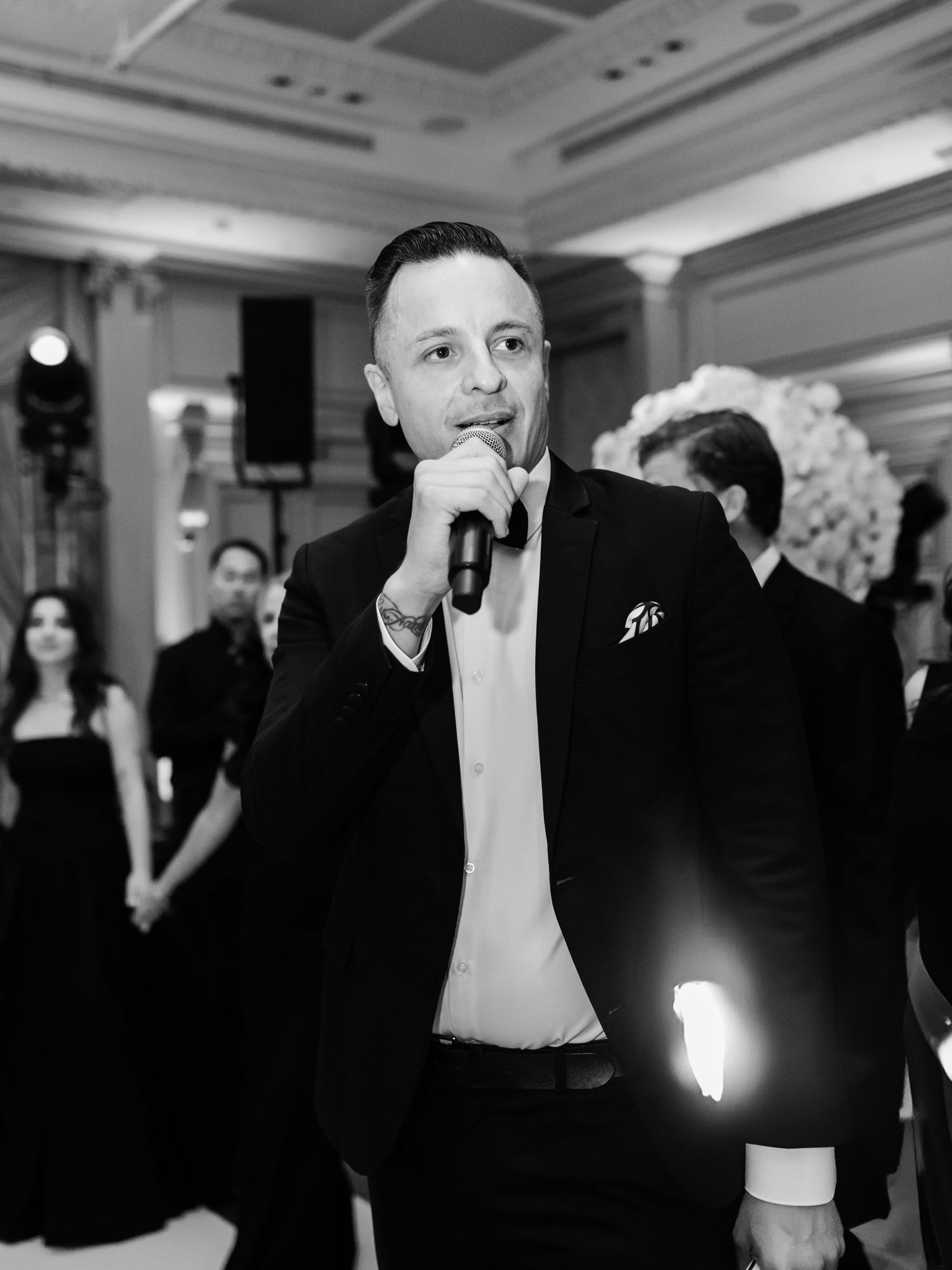 Naïm Terrache speaking into a microphone in the middle of a standing crowd, black and white