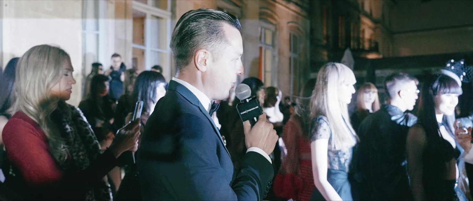 Naïm Terrache speaking into a microphone among guests at a fashion show